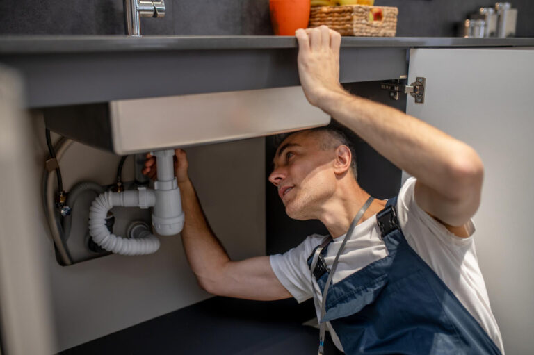 A man wearing a blue shirt fixing a sink in a kitchen